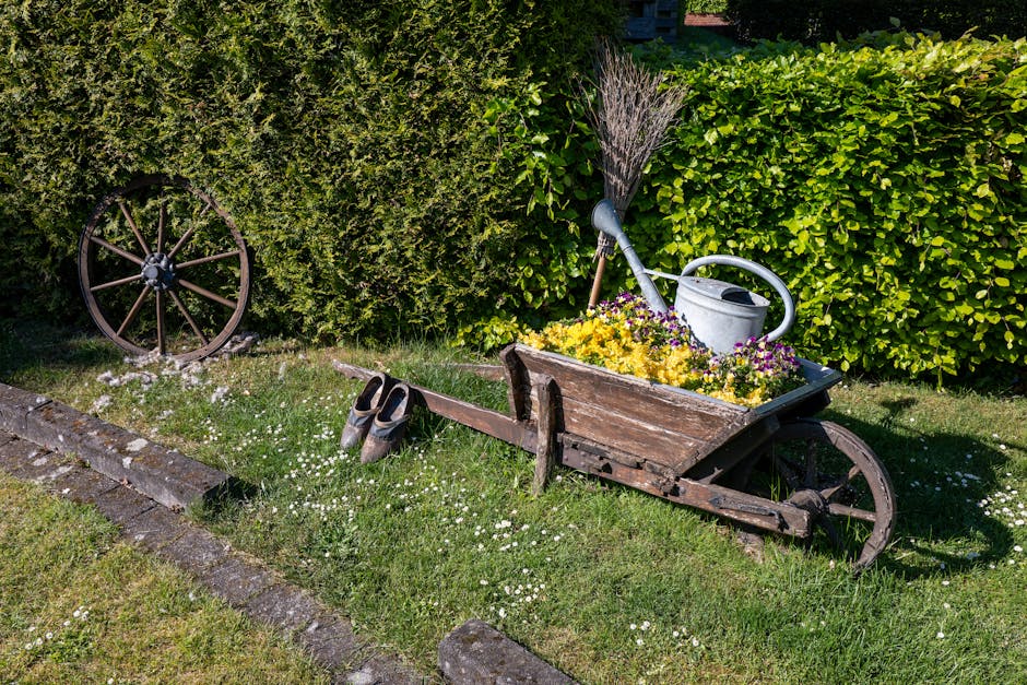 A cozy garden patio positioned against a brick house wall, featuring a weathered wooden outdoor dining table surrounded by matching wooden benches and chairs. The table is decorated with various potte